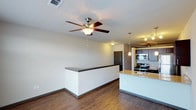 This single-story residence is designed with a contemporary, open-concept floor plan that promotes a cohesive flow between the living and kitchen areas. Hardwood-style flooring extends throughout, providing a warm, consistent aesthetic complemented by neutral-toned walls and clean architectural lines.

The kitchen is a standout feature, equipped with rich dark cabinetry, granite countertops, and a full suite of stainless steel appliances, including a gas range, built-in microwave, refrigerator, and dishwasher. A peninsula with an undermount sink and granite surface serves as both a functional workspace and a natural divider between the kitchen and living area. Pendant lighting above the peninsula and a track lighting system overhead provide focused, practical illumination throughout the space.

The living area is spacious and open, featuring a ceiling fan with a light fixture and a half-wall partition that subtly defines the space while preserving the open feel. An adjoining room benefits from a large bank of windows, flooding the space with natural light and offering views of the surrounding exterior.

The bathroom is straightforward and functional, featuring a full-sized soaking tub with an integrated shower surround, a chrome curtain rod, and hardwood-style flooring consistent with the rest of the unit.