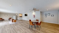 Located at 4001 Old Warren Rd in Pine Bluff, Arkansas, this single-floor community space offers a versatile and welcoming environment designed for comfort and functionality. The open-plan layout is anchored by light wood-tone flooring that runs throughout, creating a cohesive and clean aesthetic across the entire space.

The main area is generously proportioned, accommodating both a casual seating lounge and a dining area furnished with a round table and chairs. Dual ceiling fans provide consistent air circulation, while a wall-mounted flat-screen television adds a modern amenity to the space. White walls and a textured ceiling keep the interior feeling bright and neutral.

A galley-style kitchenette is tucked along one side, featuring white cabinetry on both walls, ample countertop workspace, a sink, and a full-size refrigerator — well-equipped to support gatherings or day-to-day use. A fire extinguisher station is conveniently accessible within the kitchen area.

The entry area is bright and welcoming, highlighted by a set of French doors flanked by windows that invite natural light and provide views to an outdoor patio or common area beyond. Additional windows along the perimeter further enhance the sense of openness and light throughout the space. Safety features, including a mounted fire extinguisher, are visibly integrated into the layout.