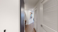 This single-floor residence offers a striking blend of industrial and contemporary design, set high above the city with expansive views of the skyline and waterfront visible from nearly every room. The open living area makes a bold architectural statement with exposed concrete columns, visible ductwork along the ceiling, and wall-to-wall black-framed windows that flood the space with natural light. Hardwood-style flooring flows throughout, anchoring the modern aesthetic. The kitchen is sleekly appointed with deep blue lower cabinets, light wood upper cabinetry, a glossy subway tile backsplash, stone countertops, and stainless steel appliances. The living and dining areas enjoy seamless access to sweeping urban and waterfront panoramas, creating an airy, loft-like atmosphere. The bedrooms continue the floor-to-ceiling window theme, offering stunning elevated views, with one bedroom featuring a wood-paneled ceiling accent and ceiling fan. The bathrooms are finished with slate-toned cabinetry, undermount sinks, stone countertops, and large-format tile flooring. A dedicated walk-in closet provides generous storage with wire shelving systems. A well-organized hallway with built-in cabinetry and louvered doors completes this thoughtfully designed, light-filled urban residence.