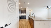 This well-appointed 1-bedroom, 1-bathroom unit offers a thoughtfully designed single-floor layout that maximizes every square foot. The open-concept kitchen and living area serves as the heart of the home, featuring warm, light hardwood-style flooring that extends throughout the main living spaces. The kitchen is a standout, showcasing dark gray shaker-style cabinetry reaching toward the ceiling, a classic white subway tile backsplash, and a large granite-topped island with an undermount sink and matte black faucet. A full suite of stainless steel appliances — including a side-by-side refrigerator, range, microwave, and dishwasher — completes this highly functional cooking space. The adjoining living area is bright and open, with recessed lighting and a clean white palette that enhances the sense of space. The bedroom offers plush carpeting, natural light from dual windows with blinds, a ceiling fan, and direct access to both a closet and the bathroom. The bathroom is finished with matching gray cabinetry, granite countertops, large-format tile surrounding the soaking tub and shower, and coordinating matte black fixtures. A dedicated closet adds practical storage to round out this move-in-ready residence.