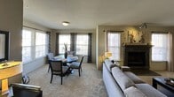 This single-floor unit offers a cohesive, well-appointed layout designed for comfortable everyday living. The open-concept living and dining area serves as the heart of the space, where a dark-framed fireplace with a decorative mantel anchors one wall, while multiple windows dressed in patterned curtains and blinds allow abundant natural light to fill the room. Plush carpeting runs throughout the living and dining areas, adding warmth underfoot. The dining area accommodates a round table with seating for four, positioned near a bay-style window arrangement that enhances the sense of openness.

The kitchen features dark espresso cabinetry paired with striking dark granite-style countertops, stainless steel appliances including a refrigerator with ice dispenser, electric range, and over-the-range microwave, complemented by durable hard-surface flooring. The bedroom is a calm retreat with carpeted floors, a ceiling fan with light fixture, and a walk-in closet accessible through a paneled door. Dark wood nightstands and warm lighting complete the relaxed ambiance.

The bathroom includes a double-sink vanity with dark cabinetry and granite countertops, a wall-mounted medicine cabinet, framed decorative artwork, and a tub-shower combination with a curtain enclosure.