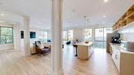 Located at 545 Bedford St in Stamford, Connecticut, this single-floor community space offers a thoughtfully designed layout that blends functionality with contemporary style. Light hardwood flooring flows throughout, complementing the bright, neutral palette that defines the interior.

The open-plan kitchen and living area serves as the heart of the space. The kitchen features stainless steel appliances, a large white quartz island with leather bar stools, open wood shelving, and globe pendant lights with gold accents that add a warm, modern touch. Floor-to-ceiling windows and sliding glass doors flood the area with natural light and provide views of the surrounding Stamford streetscape.

The lounge area is generously proportioned, with structural columns adding architectural character. It is furnished with a neutral sectional sofa, a wall-mounted flat-screen television, and accent seating — including striking blue velvet swivel chairs positioned near expansive windows that frame outdoor views of neighboring buildings and greenery.

A separate game room, finished with textured tile flooring and recessed lighting, houses a substantial wood-framed pool table with cue rack, along with contemporary wall art, creating a casual and inviting recreational retreat. A glass-paneled room divider adds a sleek, modern touch to the transition between zones. Together, these areas form a versatile and well-appointed communal environment.