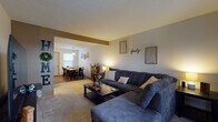 Located at 3900 Wyndover Dr in Springfield, Ohio, this two-story home offers a well-organized layout across both floors. The main level centers around an open-concept living and dining area, where the carpeted living room flows seamlessly into the dining space. A structural beam overhead subtly defines the transition between the two areas while maintaining an open, connected feel. The dining area features hardwood-style flooring, a pendant light fixture, and windows that bring in natural light, comfortably accommodating a large dining table with ample seating.

The kitchen is outfitted with white cabinetry accented by warm wood trim, a double sink, and hardwood-style flooring, providing a practical and functional cooking space. A full bathroom on this level includes a single-vanity with wood-trimmed cabinetry, a large mirror, and hardwood-style flooring.

The upper level, accessed by a staircase visible in the floor plan, hosts the bedrooms. The carpeted bedrooms offer comfortable proportions, with windows providing natural light. One bedroom is notably spacious, while an additional room offers flexibility. A separate toilet room provides added convenience. Throughout the home, neutral tones and consistent finishes create a cohesive, understated ambiance.