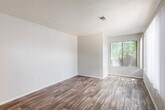 This single-floor unit offers a practical and cohesive layout designed for comfortable everyday living. Warm wood-look flooring runs throughout the space, providing a unified aesthetic that ties each area together seamlessly.

The living area is generously sized, featuring a large window fitted with vertical blinds that allows ample natural light to fill the room. A front entry door with deadbolt hardware opens directly into this space, creating a welcoming and functional entryway. Textured ceilings are present throughout, adding a subtle architectural detail overhead.

A pass-through counter connects the living and dining area to the kitchen, offering an open and interactive flow between the two spaces. The kitchen is well-appointed with white cabinetry, dark countertops, a stainless steel gas range with an overhead vent hood, a dishwasher, and a single-basin sink. The layout makes efficient use of the available space with ample upper and lower cabinet storage.

The bathroom is clean and functional, featuring a single-sink vanity with white cabinetry and a dark countertop, a full tub-shower combination, and a large mirror. The wood-look flooring continues into this room, maintaining consistency throughout the unit.

Overall, the space presents a bright, clean, and practical interior suited for a variety of living arrangements.