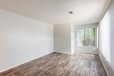 This single-floor unit offers a practical and cohesive layout designed for comfortable everyday living. Warm wood-look flooring runs throughout the space, providing a unified aesthetic that ties each area together seamlessly.

The living area is generously sized, featuring a large window fitted with vertical blinds that allows ample natural light to fill the room. A front entry door with deadbolt hardware opens directly into this space, creating a welcoming and functional entryway. Textured ceilings are present throughout, adding a subtle architectural detail overhead.

A pass-through counter connects the living and dining area to the kitchen, offering an open and interactive flow between the two spaces. The kitchen is well-appointed with white cabinetry, dark countertops, a stainless steel gas range with an overhead vent hood, a dishwasher, and a single-basin sink. The layout makes efficient use of the available space with ample upper and lower cabinet storage.

The bathroom is clean and functional, featuring a single-sink vanity with white cabinetry and a dark countertop, a full tub-shower combination, and a large mirror. The wood-look flooring continues into this room, maintaining consistency throughout the unit.

Overall, the space presents a bright, clean, and practical interior suited for a variety of living arrangements.