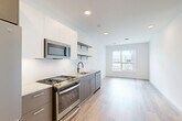 This thoughtfully designed one-bedroom, two-bathroom unit in Everett, MA offers a clean, contemporary aesthetic throughout. Light wood-toned flooring flows seamlessly across the entire space, complementing the bright white walls and recessed lighting that keep the interior feeling open and airy.

The kitchen is a standout feature, outfitted with a full suite of stainless steel GE appliances, including a gas range, over-the-range microwave, dishwasher, and refrigerator. Two-tone cabinetry pairs gray lower cabinets with white upper cabinets, accented by open metal shelving and a white tile backsplash. Light quartz countertops and a black-finish sink faucet complete the modern look.

The kitchen flows naturally into the living area, which benefits from a large window that brings in generous natural light and views of the surrounding neighborhood. The bedroom, positioned privately within the layout, also features a window with an exterior view and is served by two closets offering ample storage.

Two bathrooms round out the unit—one featuring stone-look tile flooring, a warm wood-toned vanity, and matte black hardware accents, while the second serves as a combined bathroom and laundry space for added convenience. The overall design is clean, functional, and well-suited for modern urban living.