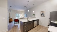 Located at 69 Marlborough Street in Portland, Connecticut, this thoughtfully designed one-bedroom, one-bathroom residence offers a efficient and modern living experience. The open-concept kitchen and living area serves as the heart of the home, featuring light hardwood-style flooring, neutral toned walls, and an abundance of natural light. The kitchen is outfitted with dark espresso cabinetry, white quartz countertops, stainless steel appliances including a full-size refrigerator, microwave, and dishwasher, and a peninsula with bar seating for three — ideal for casual dining and entertaining. Pendant lighting and a track light fixture illuminate the space stylishly. The living area opens directly onto a private balcony through a sliding glass door, offering views of the surrounding community courtyard. The bedroom is a comfortable retreat featuring a large window, warm hardwood-style flooring, and a closet. The full bathroom mirrors the kitchen's design language with dark wood cabinetry, a white quartz vanity top, a large mirror, and a tub-shower combination with clean white subway tile. The residence is part of a modern multi-story community with an expansive paved courtyard and contemporary architectural detailing.