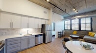 Located at Canal Bank Road in Windsor Locks, Connecticut, this single-floor unit blends industrial character with modern finishes throughout. Exposed concrete ceilings with visible ductwork and structural elements define the aesthetic, while warm hardwood flooring grounds the space with a welcoming contrast.

The open-concept kitchen and dining area form the heart of the unit, featuring two-tone gray and white cabinetry, quartz countertops, a marble-style tile backsplash, and a full suite of stainless steel appliances including a refrigerator, range, microwave, and dishwasher. A round dining table sits adjacent, framed by an original concrete accent wall that adds raw, loft-style character.

The living area benefits from a generous bank of large black-framed windows that flood the room with natural light and offer views of the surrounding neighborhood. The bedroom continues the industrial aesthetic with exposed ductwork, a concrete accent wall, and its own window with exterior views.

Two bathrooms serve the unit, each finished with light porcelain tile flooring, neutral wall tile, white vanities with ample storage, and well-lit mirrors. One bathroom includes a shower/tub combination. Clean lines and a consistent neutral palette tie the bathrooms together seamlessly with the rest of the unit's refined industrial design.