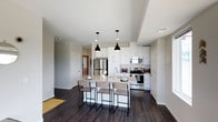 This well-appointed single-floor residence offers a thoughtfully designed open-concept layout with contemporary finishes throughout. The kitchen serves as a central highlight, featuring crisp white shaker cabinetry extending to the ceiling, granite countertops, a large island with bar seating, stainless steel appliances including a refrigerator, range, and microwave, and stylish black pendant lighting. Rich dark hardwood flooring flows consistently throughout the unit, providing a warm contrast to the neutral gray walls and white trim.

The living area is bathed in natural light through an expansive bank of corner windows, offering open views of the surrounding landscape and creating an inviting, airy atmosphere. Multiple bedrooms provide comfortable retreats, each with dark hardwood floors, generous windows with blinds, and access to closet space.

The bathroom is finished with clean white fixtures, including a full soaking tub and shower combination with a chrome grab bar. The vanity features granite countertops, white cabinetry, an undermount sink, and a large mirror framed by globe lighting, reflecting the same cohesive design language found throughout the residence. This unit combines modern aesthetics with functional living spaces in a clean, contemporary package.