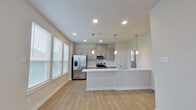 This well-appointed single-floor residence offers a thoughtfully designed layout across one bedroom, one bathroom, a combined kitchen and living area, a closet, a hallway, and a dedicated laundry room. The open-concept kitchen and living space serves as the heart of the home, featuring gray shaker-style cabinetry, a white quartz peninsula with an undermount sink, stainless steel appliances including a French door refrigerator, electric range, and microwave, as well as a subway tile backsplash. Elegant pendant lighting hangs above the peninsula, complemented by recessed ceiling lights throughout. Light-toned luxury vinyl plank flooring runs through the main living areas, adding warmth and continuity. Multiple windows fitted with horizontal blinds allow ample natural light to fill the space. The bedroom offers plush carpet flooring, a ceiling fan with light fixture, a window with an outdoor view, and access to both a closet and the full bathroom. The bathroom is finished with large-format tile flooring, a sleek white vanity with quartz countertop, and a wide mirror. The separate laundry room accommodates a full-size washer and dryer alongside a water heater, adding practical convenience to this efficiently designed home.