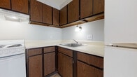 This single-floor unit offers a straightforward, functional layout with a clean, understated aesthetic throughout. The living and bedroom areas are finished with light-toned wood laminate flooring that reflects natural light streaming in through large windows dressed with vertical blinds, creating a bright and airy atmosphere. Neutral gray and beige wall tones complement the flooring, lending the space a calm, cohesive feel.

The kitchen is equipped with dark wood-grain cabinetry — both upper and lower — paired with light countertops and a stainless steel double sink. A white electric range with an overhead exhaust hood provides a functional cooking setup, and accent wall lighting adds a warm touch to the workspace.

The bathroom is well-appointed with wood-look flooring, a white vanity with under-sink storage, a mirrored medicine cabinet, and a tiled bathtub and shower surround. Dark wood-toned doors are consistent throughout the unit, adding contrast to the lighter walls and floors.

Bedroom spaces feature ample closet access, with one room showcasing a sliding door closet and another with a hinged door entry. Overhead ventilation is present throughout. The overall layout, as seen in the dollhouse view, reflects a compact yet efficiently organized single-level floor plan.