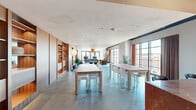 Located at 1315 Adams St in Nashville's vibrant Germantown neighborhood, this thoughtfully designed single-floor space offers an expansive, open-plan layout that seamlessly integrates multiple functional zones. Polished concrete floors run throughout, anchoring the space with an industrial warmth that complements the rich walnut wood paneling and built-in shelving found along the walls.

The living area is a standout, featuring a curated mix of seating — from plush sofas and velvet lounge chairs to sculptural accent pieces — arranged beneath an oversized woven rattan pendant light. Floor-to-ceiling steel-framed windows and glass doors flood the space with natural light while offering sweeping views of the Nashville skyline and surrounding cityscape.

The combined dining and living zone accommodates both intimate gatherings and large-scale events, with generous long communal tables paired with clean-lined white chairs, as well as a warm, round dining table surrounded by mid-century leather and cane chairs beneath a classic paper lantern pendant.

A striking glass block wall creates a dramatic architectural feature in one section, diffusing soft, ambient light while delineating zones within the open layout. A full kitchen with a central island sits at the rear. The overall ambiance is refined yet welcoming, balancing modernist design sensibility with comfortable, livable warmth.