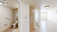 Located in Denver's Central Park neighborhood at 7401 E 26th Ave, this one-bedroom, one-bathroom residence offers a well-organized, single-floor layout designed for comfortable everyday living. Light-toned luxury vinyl plank flooring runs throughout the main areas, while the bedroom features plush wall-to-wall carpeting and a window fitted with blinds that allows natural light to filter in. The kitchen is well-appointed with warm honey-toned wood cabinetry extending to the upper walls, granite-style countertops, a full suite of white appliances including a refrigerator, electric range, and dishwasher, and a peninsula with a sink that opens to the adjacent living area. The open-concept connection between the kitchen and living room creates an efficient, cohesive space for daily use. A central hallway connects the main living areas to the bedroom and bathroom, with two closets providing ample storage. The bathroom features light wood-look flooring, accessibility grab bars, a medicine cabinet, and a clean, neutral palette. Neutral cream-toned walls throughout the residence lend a bright, airy feel. A wall-mounted thermostat in the hallway ensures climate control convenience. This thoughtfully laid-out residence delivers practical comfort in a compact and efficient footprint.