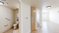 Located in Denver's Central Park neighborhood at 7401 E 26th Ave, this one-bedroom, one-bathroom residence offers a well-organized, single-floor layout designed for comfortable everyday living. Light-toned luxury vinyl plank flooring runs throughout the main areas, while the bedroom features plush wall-to-wall carpeting and a window fitted with blinds that allows natural light to filter in. The kitchen is well-appointed with warm honey-toned wood cabinetry extending to the upper walls, granite-style countertops, a full suite of white appliances including a refrigerator, electric range, and dishwasher, and a peninsula with a sink that opens to the adjacent living area. The open-concept connection between the kitchen and living room creates an efficient, cohesive space for daily use. A central hallway connects the main living areas to the bedroom and bathroom, with two closets providing ample storage. The bathroom features light wood-look flooring, accessibility grab bars, a medicine cabinet, and a clean, neutral palette. Neutral cream-toned walls throughout the residence lend a bright, airy feel. A wall-mounted thermostat in the hallway ensures climate control convenience. This thoughtfully laid-out residence delivers practical comfort in a compact and efficient footprint.