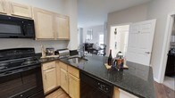 This single-floor 2-bedroom, 2-bathroom residence offers a thoughtfully designed open-concept layout that connects the kitchen, dining, and living areas in a cohesive and functional flow. The kitchen is a standout feature, showcasing rich dark granite countertops that contrast beautifully with light maple cabinetry. A deep undermount sink, built-in dishwasher, and generous counter space make it as practical as it is visually appealing. The kitchen peninsula opens directly to the dining area, which accommodates a full dining set and benefits from natural light filtering in through a window at the far end of the space. The neutral gray walls and dark hardwood-style flooring create a clean, contemporary backdrop that carries throughout the home. A barn-style door adds a touch of architectural character, providing both style and functionality. The open sightlines between rooms enhance the sense of spaciousness, making the home feel bright and inviting. The two bedrooms and two bathrooms offer comfortable and private accommodations, rounding out a residence that balances modern aesthetics with everyday livability.