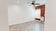 Located at 1057 S Western Ave in the heart of Los Angeles, CA, this single-floor unit blends classic character with modern updates throughout. The living area immediately draws the eye with a striking exposed brick accent wall that adds warmth and texture, complemented by crisp white walls, light wood-style flooring, and a ceiling fan with overhead lighting. Natural light filters through blinds-fitted windows, enhancing the bright and airy atmosphere.

The kitchen is thoughtfully updated with white shaker-style cabinetry, stainless steel appliances including a full-size refrigerator and built-in microwave, a dark countertop, and a sink — all set against the same exposed brick backdrop and large windows that bring in abundant natural light.

The bedroom area continues the cohesive design with matching flooring, recessed lighting, a ceiling fan, and access to a dedicated closet with a full-panel door, offering practical storage. An additional room, finished with recessed lighting and the same light wood-style flooring, provides flexible space suitable for a bedroom, office, or lounge.

The bathroom features a full soaking tub with a handheld showerhead, white subway tile surround, a single vanity with sink, and a window for natural ventilation. The overall design is clean, functional, and welcoming.