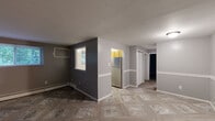 Located at 314 E 24th St in Chester, PA, this two-bedroom, one-bathroom unit offers a straightforward single-floor layout designed for comfortable, efficient living. The living room is finished with a distinctive patterned tile floor and neutral two-tone gray walls accented by white chair-rail molding, creating a clean and cohesive look. Windows allow natural light to filter in, contributing to an open feel within the space. A pass-through window connects the living area to the kitchen, which features light wood cabinetry, a stainless steel refrigerator, a range, tiled backsplash, and matching patterned flooring that continues from the main living area. The primary bedroom is a generously sized room with dark carpeting, two closets, and access to the hallway, providing ample storage. The second bedroom is also carpeted and includes a window with views of surrounding greenery, along with a baseboard heating unit. Both bedrooms are painted in deep gray tones, lending a modern, understated aesthetic. The bathroom includes a full bathtub with a clean white surround. Baseboard heating is present throughout the unit, and the hallway connects all rooms efficiently. The overall ambiance is neutral and move-in ready.