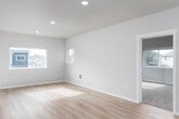 This two-story home presents a clean, modern aesthetic defined by neutral tones, white trim, and consistent finishes across both floors. The main level features light wood laminate flooring that flows through the open living areas and hallways, creating a cohesive and bright atmosphere. Recessed lighting and pendant fixtures illuminate the space effectively throughout.

The kitchen serves as a functional centerpiece, featuring a large white island with an integrated sink, crisp white cabinetry extending to the ceiling, white quartz countertops, and a full suite of stainless steel appliances including a refrigerator, electric range, and microwave. The open layout connects the kitchen seamlessly to the living area, which offers windows with views of the surrounding neighborhood.

Bedrooms are carpeted for comfort and include windows that bring in natural light. The primary bedroom benefits from dual corner windows, providing views of the exterior. A dedicated bathroom on this level includes a walk-in shower with sliding glass doors, a white vanity, and wood-tone flooring. A second full bathroom features a soaking tub and shower combination, a white vanity with chrome hardware, and matching flooring. Double-panel closet doors and ample hallway storage add to the home's practical layout.