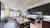 Located at 13535 Lyndhurst St in Austin, TX, this thoughtfully designed one-bedroom, one-bathroom residence offers an efficient and elegant single-floor layout. The open-concept kitchen and living area serves as the heart of the home, where dark espresso cabinetry with under-cabinet lighting contrasts beautifully against granite countertops. A central kitchen island with bar seating and pendant lighting provides both prep space and a casual dining option. Stainless steel appliances, a subway tile backsplash, and a built-in desk area with ample cabinetry complete the kitchen's functional design. Track lighting overhead adds a modern touch. Light wood-style flooring flows seamlessly throughout, creating a cohesive and airy feel. The living room is bathed in natural light from large windows and a set of glass French doors, adding warmth and an outdoor connection. The bedroom offers a comfortable retreat with generous windows, light-filtering blinds, and neutral tones. The bathroom features a granite-topped vanity with dark cabinetry, a soaking tub with shower, large-format tile flooring, and a well-lit mirror. A dedicated closet and entrance complete this well-appointed residence.