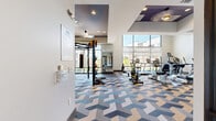 Located at 2007 Knoll Top Ln in Franklin, TN, this fitness center offers a generously sized, single-floor workout facility designed to accommodate a wide range of exercise disciplines. The space is immediately distinguished by its bold, geometric-patterned carpet in shades of blue, gray, and beige, which adds a modern aesthetic throughout the room.

Floor-to-ceiling windows line one side of the facility, flooding the interior with abundant natural light and providing open views of the surrounding outdoor amenity area, including a pool and neighboring buildings. The expansive glazing creates an airy, energizing atmosphere well-suited for an active environment.

The layout is thoughtfully divided into functional zones. A cardio area features a variety of machines including treadmills, ellipticals, stationary bikes, and a rowing machine. A dedicated functional training zone houses a multi-station rig equipped with TRX suspension trainers, gymnastic rings, battle ropes, kettlebells in multiple weights, and a punching bag. A free weight section includes a full dumbbell rack and adjustable benches. Additional strength machines round out the equipment offering. Built-in shelving stores yoga mats and accessories, and a water fountain station is conveniently positioned for easy access. Recessed and pendant lighting complements the natural light, ensuring the space is well-lit at all hours.