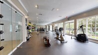 Located at 5825 Crossings Blvd in Antioch, TN, this fitness center offers a comprehensive, single-floor exercise facility designed to support a wide range of workout routines. The space is generously sized, providing ample room for both cardio and strength training activities without feeling crowded.

Large, white-framed windows line one side of the room, allowing abundant natural light to pour in and offering pleasant views of the surrounding greenery. This connection to the outdoors contributes to an open, energizing atmosphere. Recessed lighting throughout the ceiling ensures the space remains well-lit at all hours.

The exercise room is outfitted with a diverse array of cardio equipment, including treadmills, elliptical trainers, a stationary bike, a stair climber, and a rowing machine. A dedicated free weights area features a full rack of dumbbells alongside an adjustable bench and medicine balls, supported by floor-to-ceiling mirrors that span an entire wall — ideal for maintaining proper form. A cable machine further rounds out the strength training options.

Durable rubber flooring covers the entire exercise area, providing both comfort and safety. Crown molding and neutral-toned walls lend a polished, refined aesthetic to the space. A glass-paneled interior partition adds a modern architectural touch, while a posted fitness center rules board reflects attentive facility management.