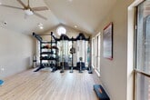 Located at 3415 Havenbrook Dr in Houston, TX, this fitness center is a thoughtfully designed facility that offers a complete workout experience. The space is divided into two connected exercise areas, unified by light hardwood flooring and a warm, neutral color palette throughout.

The primary workout area is defined by its striking vaulted ceiling with a distinctive circular porthole window that floods the room with natural light. A ceiling fan adds comfort during workouts, while recessed lighting ensures visibility at all hours. Large windows along the walls provide additional natural light and outdoor views. This area is well-appointed with a multi-functional cable machine system, a weight rack stocked with medicine balls and dumbbells, and a step platform, catering to a wide range of strength training needs.

The secondary workout area features the same soaring vaulted ceiling with a ceiling fan and accommodates cardio equipment including a stationary bike and treadmill, along with a dumbbell rack and adjustable bench — ideal for versatile training routines.

Supporting the fitness areas is a small kitchenette equipped with a sink, countertop, cabinetry, and a full-size refrigerator. Two restrooms with hardwood-style flooring offer convenient facilities for users. A posted fitness center rules board ensures a well-managed, community-friendly environment.