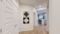 This single-floor residence offers a well-designed, open-concept layout with light wood-style flooring that flows consistently throughout the space. The entryway makes a welcoming first impression, featuring a paneled closet door and clean white walls accented by decorative geometric wall art.

The kitchen serves as a central hub of the home, outfitted with gray shaker-style cabinetry, white quartz countertops, a subway tile backsplash, and a full suite of stainless steel appliances including a French door refrigerator, range, microwave, and dishwasher. A generously sized center island with seating provides additional prep and dining space, illuminated by a pair of modern metallic pendant lights.

The living area is warm and inviting, highlighted by large windows and a glass door that open to a private balcony, allowing abundant natural light. A ceiling fan adds comfort overhead.

The bedroom is a calm retreat, featuring windows with outdoor views, a ceiling fan, and ample natural light. It connects to a spacious walk-in closet equipped with multi-level wire shelving for organized storage.

The bathroom is functional and clean in design, featuring a white vanity with drawers, light countertops, a full soaking tub with tiled surround, and a patterned shower curtain adding a subtle decorative touch.