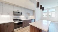 Located at 1445 Town Center Dr in Chula Vista, CA, this modern two-story home offers four bedrooms and two bathrooms with a thoughtfully designed open layout. The kitchen is a standout feature, boasting two-tone cabinetry with white upper cabinets and rich walnut-finish lower cabinets, a classic white subway tile backsplash, quartz countertops, a central island, and a full suite of stainless steel appliances. Soaring ceilings amplify the sense of space, while sleek cylindrical pendant lights add a contemporary touch. The living area benefits from tall windows that invite abundant natural light and provide views of the surrounding neighborhood. Light hardwood flooring runs throughout the main living spaces, creating a warm, cohesive aesthetic. The bedrooms offer a comfortable retreat, with some featuring soft carpeting. The primary bedroom is generously sized with vaulted ceilings and direct access to a well-appointed en-suite bathroom. Both bathrooms are finished with floating walnut-toned vanities, quartz countertops, undermount sinks, and matte black fixtures. The primary bath includes a dual-sink vanity and a glass-enclosed walk-in shower with built-in shelving, reflecting a clean, modern design sensibility throughout the home.