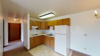 Located at 1305 Walker Ave NW in Grand Rapids, Michigan, this single-floor unit offers a straightforward, functional layout with clearly defined living spaces. The kitchen is arranged in an L-shaped configuration and is equipped with warm oak-toned cabinetry extending to the upper and lower walls, light-colored countertops, a coil cooktop, a stainless steel sink, and a full-size refrigerator. A ventilation hood is mounted above the cooktop, and tile flooring runs throughout the kitchen area, providing a practical, easy-to-clean surface.

The living area flows directly from the kitchen and features neutral-toned carpeting and a modest chandelier overhead, lending the space a simple, welcoming character. Windows allow natural light to enter, offering views of the surrounding neighborhood. The bedroom spaces are similarly carpeted and bright, each featuring windows with blinds that admit ample daylight. Wall-mounted vents indicate a central air and heating system throughout.

The bathroom is equipped with a single-sink vanity with wood cabinetry beneath, a large mirror with overhead lighting, a tiled tub-and-shower combination with grab bars, and tile flooring. The overall design of the unit is clean and utilitarian, with neutral walls and consistent finishes across all rooms.