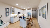 This thoughtfully designed single-floor residence offers a seamless blend of modern aesthetics and functional living. The heart of the home is a gourmet kitchen showcasing crisp white shaker cabinetry, granite countertops, stainless steel appliances including a gas range, built-in microwave, and a French door refrigerator with ice dispenser. A central island with pendant lighting provides additional prep space and casual seating with woven bar stools, making it ideal for entertaining. Light wood-style flooring flows throughout, enhancing the bright, airy feel of the space. The open-concept living area transitions naturally from the kitchen, featuring neutral toned walls that complement the contemporary décor. The bedroom is a calm retreat with a large window that brings in natural light and offers exterior views. The primary bathroom is finished with large-format tile flooring, a glass-enclosed walk-in shower, a granite-topped double vanity, and direct access to a walk-in closet. A secondary bathroom provides additional convenience with matching granite counters and clean, modern fixtures. Recessed lighting and thoughtful storage solutions, including multiple panel doors and built-in cabinetry, complete this well-appointed residence.