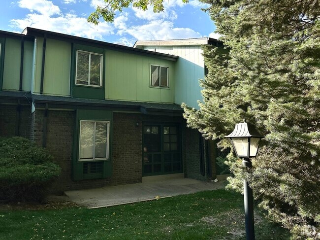 Inviting green townhouse with brick accents and lush landscaping. - Char Rose