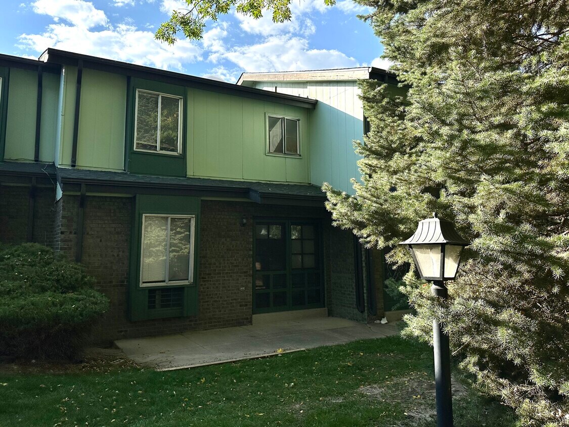Inviting green townhouse with brick accents and lush landscaping. - Char Rose