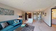 This single-floor residence offers a thoughtfully laid-out interior designed for comfortable everyday living. The open-concept living and dining area serves as the heart of the home, featuring soft wall-to-wall carpeting, a textured ceiling, and a large sliding glass door that invites natural light into the living room. The dining area is defined by an elegant chandelier and is positioned adjacent to the living space, creating a seamless flow for entertaining.

The galley-style kitchen is lined with rich dark wood cabinetry on both sides, providing generous storage and counter space. It is equipped with full appliances including a range, refrigerator, dishwasher, and sink, all set atop durable tile flooring.

The primary bedroom is generously sized with plush carpet, dual windows that allow natural light, and ample space for a full furniture arrangement. A second bedroom features louvered closet doors and comfortable proportions. Both rooms offer a calm, restful ambiance.

Two bathrooms serve the residence — one featuring a full tub and shower combination with mosaic tile flooring, and another with a wide vanity, large mirror, and well-lit fixtures. Dark wood doors provide a consistent design accent throughout the home, complementing the neutral walls and light-toned finishes.