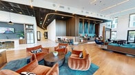 This impressive 2,190 square foot clubroom, located at 10 Tower St NW in Atlanta, GA, showcases a blend of contemporary design and functional elegance. The space is defined by its soaring ceilings and expansive floor-to-ceiling windows, which flood the area with natural light and provide panoramic views of the Atlanta skyline.

The interior is thoughtfully divided into various zones, each serving a distinct purpose. A central lounge area features comfortable seating options, including plush sofas and stylish armchairs in rich, warm tones. The polished wooden flooring throughout adds warmth and continuity to the space.

A striking design element is the geometric patterned flooring in the entrance area, creating visual interest and delineating different functional spaces. Modern lighting fixtures, including pendant lights and recessed ceiling lights, enhance the ambiance and provide flexible illumination options.

The clubroom also includes a sleek kitchenette area with a marble countertop and bar seating, perfect for casual gatherings or events. Architectural details such as wooden slat walls and accent colors in teal and coral add depth and character to the space.

Multiple seating arrangements cater to different group sizes and activities, from intimate conversations to larger social gatherings. The overall design aesthetic balances modern minimalism with inviting textures and colors, creating a sophisticated yet welcoming environment for residents and guests alike.