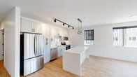 Unit 217 at 2215 Hickory St in St. Louis, Missouri presents a thoughtfully designed single-floor residence with a clean, contemporary aesthetic throughout. The open-concept kitchen is a standout feature, showcasing white shaker cabinetry, stainless steel appliances including a refrigerator, range, microwave, and dishwasher, complemented by a white center island. Black track lighting and globe pendant fixtures illuminate the space, while light hardwood-style flooring extends through the kitchen and living areas, creating a cohesive, bright atmosphere. Windows fitted with roller shades allow natural light to filter in.

The living area is generously proportioned, with recessed lighting and a seamless flow from the kitchen. A well-lit hallway connects the main living spaces to the private areas of the unit, featuring glass-accented doors that add a modern touch.

The bedrooms offer neutral carpet flooring and include closet storage, providing comfortable, quiet retreats. Two bathrooms serve the unit: one features a walk-in glass-enclosed shower with tile surround, while the second includes a full soaking tub with a tile-accented surround, both finished with white vanities and light tile flooring. The overall design is clean, modern, and move-in ready.