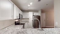 Located at 405 Thomas Burke Dr in Hillsborough, NC, this single-floor residence offers a well-designed layout with contemporary finishes throughout. The kitchen is a standout feature, equipped with white shaker-style cabinetry, granite countertops with subtle veining, a subway tile backsplash, and a full suite of stainless steel appliances including a refrigerator, electric range, and over-the-range microwave. A peninsula with a modern industrial-style faucet provides additional prep space and casual seating potential. Track lighting illuminates the kitchen efficiently. The open living area flows seamlessly from the kitchen, showcasing light-toned luxury vinyl plank flooring and neutral wall tones that create a bright, welcoming atmosphere. A ceiling fan adds both comfort and style. Bedrooms offer a mix of hardwood-style and carpeted flooring, each with ceiling fans and windows that let in natural light with views of surrounding greenery. The bathrooms are finished with white cabinetry, brushed nickel hardware, wood-look flooring, and clean, neutral palettes. One bathroom features a soaking tub with a built-in linen tower for added storage. The overall design emphasizes clean lines, neutral tones, and functional living throughout.