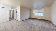 Located at Manor Village in Bath, NY, this two-bedroom, one-bathroom unit offers a practical and well-organized single-floor layout. The combined living and dining area is generously proportioned, featuring neutral wall-to-wall carpeting, clean white walls, warm wood-toned baseboards, and a chandelier overhead. Natural light filters in through multiple windows fitted with blinds, and baseboard heating runs throughout the unit. A hallway connects the main living space to the rest of the unit, providing a clear and functional flow between rooms. The galley-style kitchen is efficiently arranged with gray cabinetry, light countertops, a double-basin sink, a dishwasher, a range, and a refrigerator. Tile flooring and a window overlooking the outdoors complete the kitchen. The primary bedroom is a comfortable size, offering carpeting, a wall-mounted A/C unit, a window with natural light, and a baseboard heater. The second bedroom is bright and cozy, also carpeted with a window view. Three closets throughout the unit provide ample storage. The bathroom features a full-size soaking tub and shower combination with a grab bar for added accessibility. Overall, this unit offers a clean, straightforward layout well-suited for everyday living.