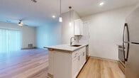 Located at 6386 Transit Rd in Depew, NY, this single-floor unit offers a clean, contemporary design with thoughtfully selected finishes throughout. The kitchen serves as a central highlight, featuring white shaker cabinetry with brushed nickel hardware, granite countertops, a subway tile backsplash, stainless steel appliances including a refrigerator and range, and a peninsula island with an undermount sink illuminated by stylish pendant lighting. Light hardwood flooring flows seamlessly through the kitchen and main living areas, creating a bright and cohesive aesthetic. The living area is generously sized, equipped with a ceiling fan and a sliding glass door dressed in vertical blinds that allows natural light to fill the space. Bedrooms are finished with plush wall-to-wall carpeting, ceiling fans, and windows with blinds that bring in additional natural light, offering a comfortable and quiet retreat. The bathroom mirrors the kitchen's design language with white cabinetry, granite countertops, a large vanity mirror, and coordinating light hardwood flooring. Neutral wall tones throughout the unit create a versatile backdrop ready for personalization. The overall ambiance is modern, fresh, and move-in ready.