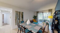 Located at 1517 Cameron Samuel Ln in West Palm Beach, FL, this well-designed 2-bedroom, 2-bathroom residence offers a comfortable and functional single-floor layout. The entry hallway, accented by a bold teal feature wall, sets a vibrant tone and opens into a combined dining, kitchen, and living area. The kitchen is equipped with rich walnut cabinetry, dark granite countertops, stainless steel appliances, a breakfast bar peninsula, tile flooring, and convenient in-unit laundry just steps away. The open dining and living space is bright and inviting, featuring large sliding glass doors that flood the area with natural light and provide direct access to a private balcony with lush outdoor views. The living room showcases a striking teal accent wall, adding depth and character to the space. Both bedrooms are carpeted for comfort, each with its own closet — including a spacious walk-in closet in the primary suite. The primary bedroom is generously sized, offering a tranquil retreat. The bathrooms are cleanly finished, with one featuring a sleek glass-enclosed walk-in shower, granite vanity, and neutral tile work. This residence combines modern finishes with a warm, coastal-inspired aesthetic throughout.