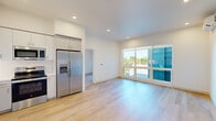 Located at 7007 SW Hampton St in Tigard, Oregon, this modern single-floor residence offers three bedrooms and two bathrooms thoughtfully arranged within a bright, efficiently designed layout. Light-toned hardwood flooring runs throughout the home, creating a cohesive and contemporary feel from room to room.

The open-concept kitchen and living area serves as the heart of the home. The kitchen is equipped with a full suite of stainless steel GE appliances, including a side-by-side refrigerator with ice and water dispenser, an electric range, over-the-range microwave, and dishwasher. White flat-panel cabinetry extends to the ceiling, paired with clean white countertops and a classic subway tile backsplash. The living area benefits from large picture windows that invite abundant natural light and provide open outdoor views.

The primary bedroom features a wall of oversized windows and a dedicated en-suite bathroom with a glass-enclosed walk-in shower, a vanity with built-in shelving, and light wood flooring. A second full bathroom offers a tub-shower combination with white subway tile surround. Additional bedrooms are well-proportioned, each with natural light and individual closets with built-in shelving. The home also features a wall-mounted mini-split HVAC system for personalized climate control and recessed lighting throughout.