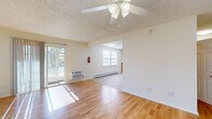 This single-floor space offers a practical and comfortable layout with a clean, neutral aesthetic throughout. The living area is bright and open, featuring light hardwood flooring, a ceiling fan, and a sliding glass door that allows generous natural light and outdoor views. Baseboard heating is present throughout the unit, ensuring consistent warmth. An adjacent area, visible through a connecting opening, includes a pair of double-hung windows fitted with blinds, providing additional natural light.

The kitchen is well-appointed with warm oak cabinetry offering ample upper and lower storage, dark laminate countertops, and a full suite of white appliances including a range, dishwasher, and refrigerator. A ventilation hood over the range and a double window overlooking the dining area add both function and light to the space. Durable tile flooring completes the kitchen.

The bedrooms each feature light hardwood flooring and ceiling fans, with baseboard heating and windows overlooking greenery. One bedroom includes a closet with built-in shelving. The bathroom is finished with neutral stone-look tile on both the floor and tub surround, complemented by a white vanity with storage and a full soaking tub with a curved shower rod.