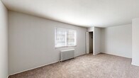 Located at 4212 Allendorf Dr in Cincinnati, Ohio, this single-floor unit offers a straightforward, functional layout distributed across several connected rooms. The living area is generously sized, featuring neutral-toned carpet, soft white walls, and a window fitted with blinds that allows natural light to filter in. A classic cast-iron radiator beneath the window serves as the primary heat source, adding a traditional character to the space. An open closet with a rod provides convenient built-in storage directly off this room.

A second carpeted room mirrors a similar layout, featuring its own radiator, a window-mounted air conditioning unit, and a ceiling fan with integrated lighting—providing both comfort and ventilation year-round. This room also benefits from natural light through a window with blinds.

The entry area transitions from tile to carpet, providing a natural threshold into the living spaces. The kitchen is equipped with warm wood-toned cabinetry, dark laminate countertops, a double-basin sink, a white electric range, and tile flooring—offering a practical cooking environment with a window for natural light.

The bathroom includes a tiled tub and shower combination, a window for ventilation, stone-look tile flooring, and standard fixtures, presenting a clean and functional space throughout.