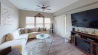 This single-floor residence offers a thoughtfully designed open-concept layout that connects its main living spaces with ease. Neutral gray walls and light wood-look flooring flow throughout, creating a cohesive and inviting atmosphere across the home.

The living room is generously sized, featuring a ceiling fan, a sliding glass door that brings in natural light, and ample space for a large sectional sofa. An adjoining sitting area provides additional flexibility for relaxing or entertaining. The dining area nearby is highlighted by a stylish chandelier overhead and tray ceiling detail, offering a warm setting for gathering around a farmhouse-style table.

The kitchen is well-equipped with dark espresso cabinetry, granite countertops, stainless steel appliances including a gas range and built-in microwave, and light wood-look flooring. A pass-through layout connects the kitchen efficiently to the dining and living spaces.

The primary bedroom is carpeted and spacious, featuring a ceiling fan and window with natural light. It connects directly to a private bathroom with wood-look flooring, dark vanity cabinetry, granite countertops, and access to a walk-in closet. A second bathroom includes a tub and shower combination with wood-look flooring and additional vanity storage.
