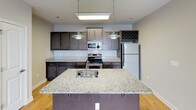 This single-floor residence offers a thoughtfully designed layout that balances comfort and functionality. The open-concept living and kitchen area serves as the heart of the home, where warm hardwood-style flooring transitions seamlessly into plush carpeting. The kitchen is a standout space, featuring rich dark cabinetry, granite countertops, stainless steel appliances, and a central island with a built-in sink and pendant lighting overhead — ideal for both everyday cooking and casual entertaining. A dedicated wine rack adds a refined touch to the cabinetry. The living area benefits from a ceiling fan and an elevated tray ceiling detail, enhancing the sense of openness. The bedrooms are generously sized, finished with neutral carpet and large windows that invite natural light and outdoor views. One bedroom includes access to a spacious walk-in closet outfitted with wire shelving and a built-in shelving unit, providing ample storage. Both bathrooms are finished with granite-topped dark vanities and full tub-shower combinations. Neutral warm tones carry throughout the home, creating a cohesive and inviting ambiance. Additional utility space with an electrical panel rounds out this well-organized and comfortable residence.