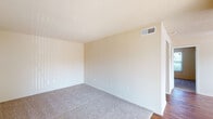 This single-floor space offers a practical and straightforward layout designed for comfortable everyday living. The living area is finished with plush wall-to-wall carpeting and neutral-toned walls, creating a clean and versatile backdrop. A large sliding glass door fitted with vertical blinds allows natural light to fill the space and provides access to the exterior. The kitchen is well-equipped with white cabinetry offering ample upper and lower storage, speckled laminate countertops, a double-basin stainless steel sink, a coil-burner electric range, and a full-size refrigerator. A range hood overhead adds functional ventilation. The bedroom features soft carpeting, a window with blinds that brings in natural light, and direct access to the bathroom. The bathroom is appointed with wood-look flooring, a white vanity with cabinet storage, and leads to a dedicated bathtub and shower area. An adjacent built-in shelving unit provides additional organized storage. Throughout the space, textured ceilings, HVAC vents, and consistent neutral finishes contribute to a cohesive, move-in-ready environment.