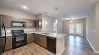 This single-story, 3-bedroom, 2-bathroom home offers a thoughtfully designed open-concept layout with modern finishes throughout. The kitchen is a standout feature, equipped with dark wood cabinetry, granite-look countertops, black appliances including a refrigerator, range, microwave, and dishwasher, and a peninsula island with pendant lighting above. Wood-look flooring runs through the kitchen and living areas, creating a seamless flow toward the living room, which is brightened by a ceiling fan and accessed through French doors leading to an outdoor space. The neutral, warm-toned walls throughout lend a cohesive and inviting ambiance. The bedrooms feature plush carpeting and ceiling fans, offering a comfortable retreat. The primary bedroom includes an en-suite bathroom with dark wood vanity cabinetry, dual sinks, and countertop space, as well as a dedicated walk-in closet outfitted with wire shelving for organized storage. A second walk-in closet with wire shelving provides additional storage capacity. The bathrooms reflect the same modern aesthetic with clean lines and practical fixtures. Natural light filters in through multiple windows, enhancing the open and airy feel of this well-planned home.