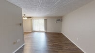 Located at 225 Alcoma Blvd in Pittsburgh, PA, this one-bedroom, one-bathroom unit offers a practical and comfortable layout across a single floor. The open-concept living area features wood-look laminate flooring and a ceiling fan with light fixture, creating a bright and airy atmosphere. Large windows allow natural light to fill the space, while a baseboard heating system ensures warmth throughout. The kitchen opens directly to the living room via a pass-through counter and is equipped with warm wood-toned cabinetry, marble-look countertops, a stainless steel sink, a dishwasher, a white electric range, and a full-size refrigerator — providing ample storage and functionality. The spacious bedroom is carpeted for comfort and includes a large double-door louvered closet, a window with outdoor views of surrounding greenery, and a wall-mounted air conditioning unit. The full bathroom features a white tiled tub and shower surround with a grab bar, offering clean, classic finishes. A hallway connects the main living areas, completing the efficient and well-organized floor plan. The textured ceilings throughout add a subtle architectural detail consistent across the unit.