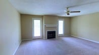 Located at 501 Fairways Dr in Vicksburg, Mississippi, this single-story home offers a comfortable and well-appointed living space. The main living area is a standout feature, showcasing a centrally positioned fireplace with a classic white mantel and tile hearth, flanked symmetrically by two white-framed glass panel doors that flood the room with natural light. The warm, neutral-toned walls complement the plush wall-to-wall carpeting, creating an inviting and cohesive atmosphere throughout. A ceiling fan is installed overhead, adding both functionality and a traditional touch to the space. The open layout of the living area provides a generous sense of space, making it well-suited for both everyday living and entertaining. The consistent use of white trim and millwork throughout adds a clean, classic finish to the interior. The symmetrical design of the main living room, with its balanced door and fireplace arrangement, gives the home a structured and thoughtfully designed aesthetic. Overall, this property combines practical single-floor living with charming architectural details in a residential Vicksburg neighborhood.