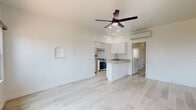 This single-floor space offers a clean, modern aesthetic defined by light-toned luxury vinyl plank flooring, crisp white walls, and recessed lighting throughout. The open-concept living and kitchen area forms the heart of the space, where a peninsula with granite countertops serves as both a functional workspace and a natural divider. The kitchen is well-equipped with white shaker cabinetry, stainless steel appliances including a gas range and refrigerator, and an under-cabinet range hood. A wall-mounted mini-split system provides efficient climate control, while a ceiling fan with integrated lighting adds comfort and character to the living area. A charming arched wall niche adds a subtle architectural detail to the living space. The bedroom is generously sized and similarly appointed with its own ceiling fan and mini-split unit, offering direct views into the adjoining bathroom area. The bathroom is a standout feature, showcasing bold black-and-white patterned floor tile, marble-look wall tile in the walk-in shower, granite countertops on the white vanity, and brushed gold fixtures that lend a sophisticated, designer touch. Natural light filters in through a window, brightening the space. Overall, the unit presents a cohesive, well-appointed interior with thoughtful finishes.