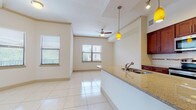 This single-floor unit is designed with an open-concept layout that seamlessly connects the kitchen, dining, and living areas. The kitchen is a standout feature, equipped with rich dark wood cabinetry, granite countertops, stainless steel appliances including a refrigerator, electric range, and built-in microwave, as well as a tile backsplash. A central island with a built-in sink and pendant lighting in amber tones serves as both a functional workspace and a visual focal point.

Large-format polished tile flooring extends throughout the main living areas, reflecting natural light that enters through multiple windows fitted with horizontal blinds. The living area is generously proportioned, with a ceiling fan and track lighting adding to the room's functionality. Crown molding accents the ceiling, lending a refined touch to the space.

The bedroom features neutral carpeting and a window with outdoor views, creating a comfortable and quiet retreat. The bathroom is well-appointed with a wide double-sink vanity topped with granite, dark wood cabinetry, and tile flooring consistent with the rest of the unit. Throughout, the warm cream-toned walls and clean design maintain a cohesive, light-filled ambiance.